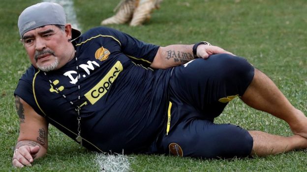 Diego Maradona rests on the ground after delivering training